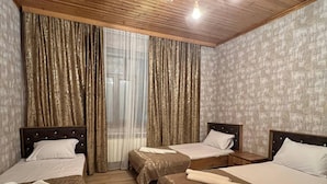A hotel room with two beds, wooden flooring, a ceiling fan, and a window with curtains.