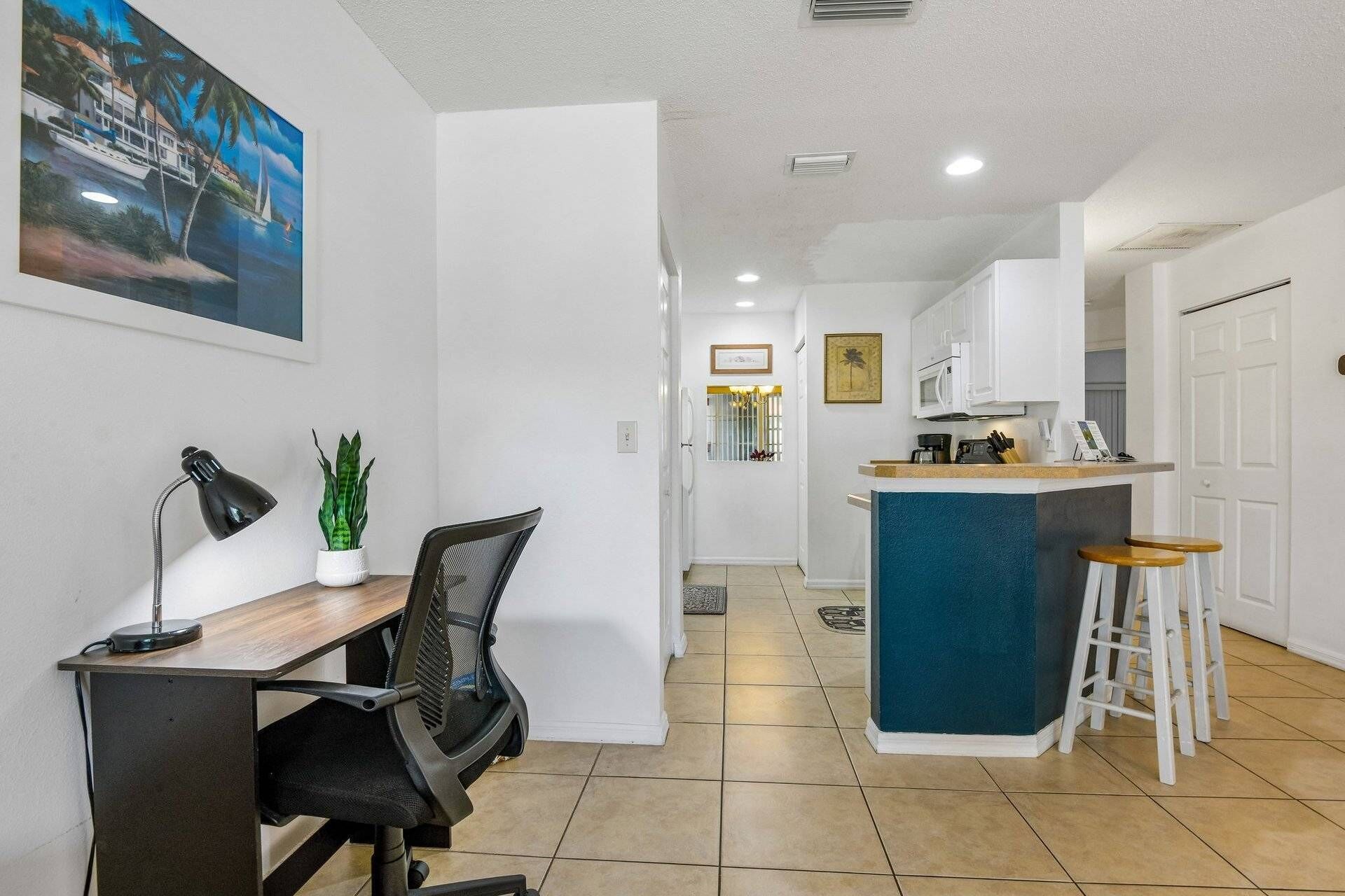 A modern kitchen with white cabinets, a blue island, and a bar area with stools.