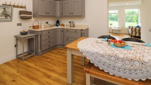 A modern kitchen with grey cabinets, a wooden table with a lace tablecloth, and a view of the garden through a window. - THE FARM COTTAGE, family friendly in Athy, County Kildare (Athy)