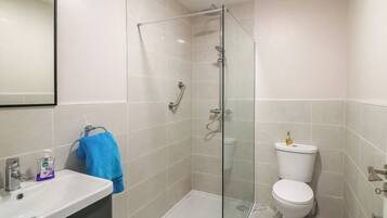 Un bany modern amb dutxa envidriada, vàter blanc i un lavabo amb dispensador de sabó.