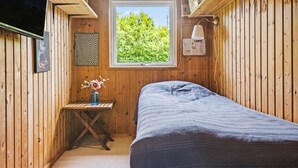 A small wooden room with a bed, a window with a view of greenery, a small table with a vase, and a wall-mounted lamp. - 2 bedroom amazing home in Stege (Stege)