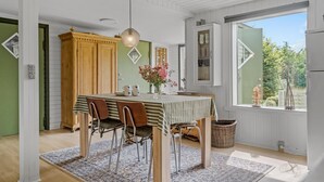 A dining area with a table set for four, surrounded by chairs, a hanging light fixture, and a view of greenery through a window. - 2 bedroom amazing home in Stege (Stege)