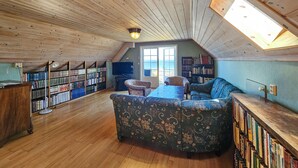 A cozy attic room with a wooden ceiling, a large window, a sofa, and bookshelves filled with books. - Nice home in åsgårdstrand (Åsgårdstrand)