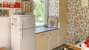 A compact kitchen with a refrigerator, a window, and a floral-patterned wall.