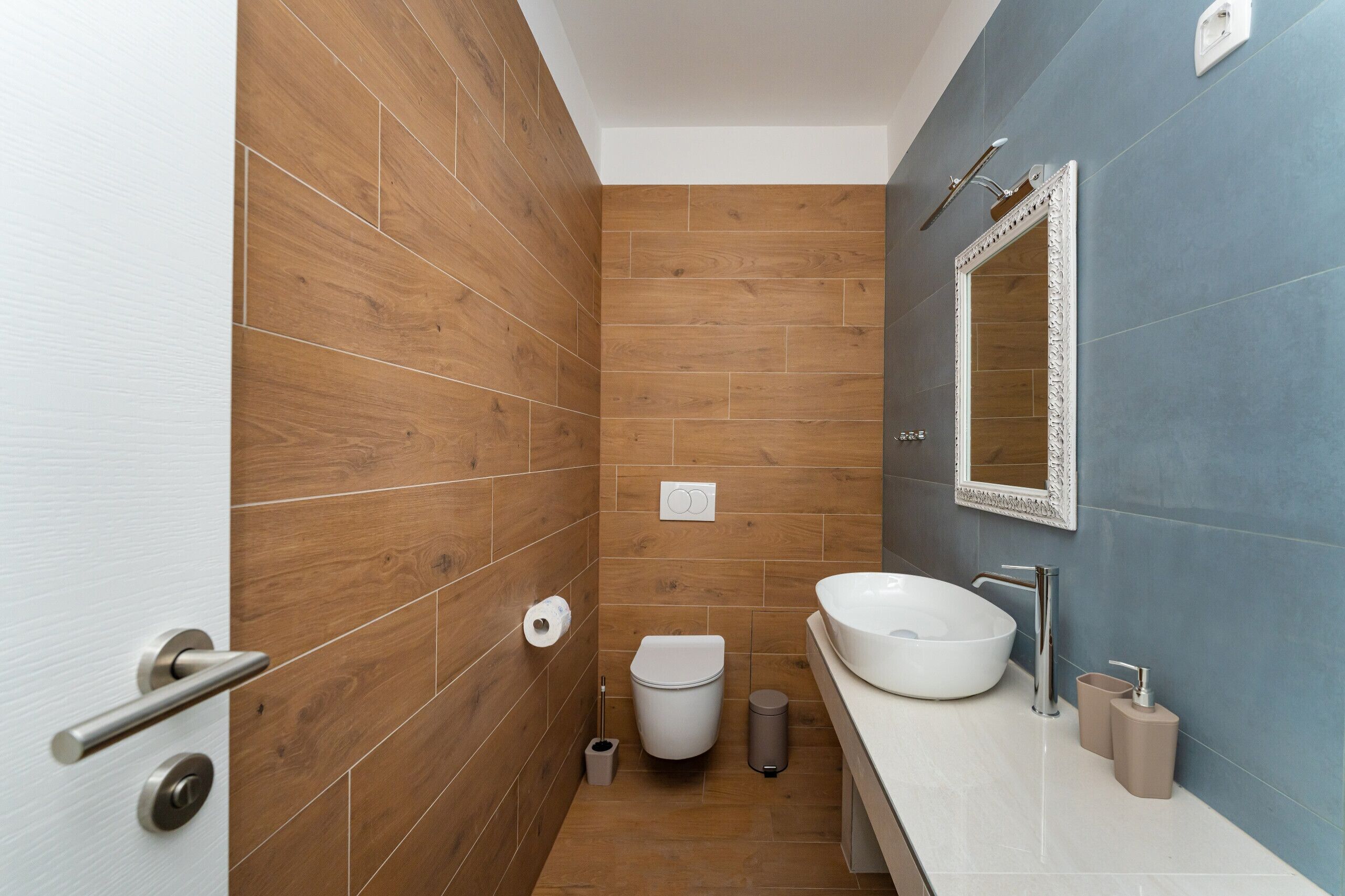 Een moderne badkamer met een houten vloer, een witte wastafel en een spiegel met decoratieve lijst.