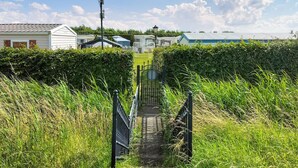 Een pad dat leidt naar een rij gemoderniseerde kampeerwoningen, met een metalen poort en een betonnen paal.