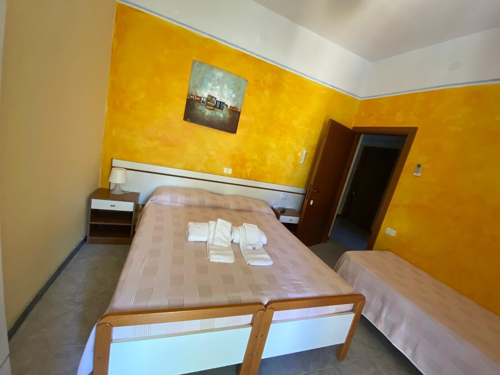 Een slaapkamer met een bed, nachtkastjes, een bankje en een schilderij aan de muur.