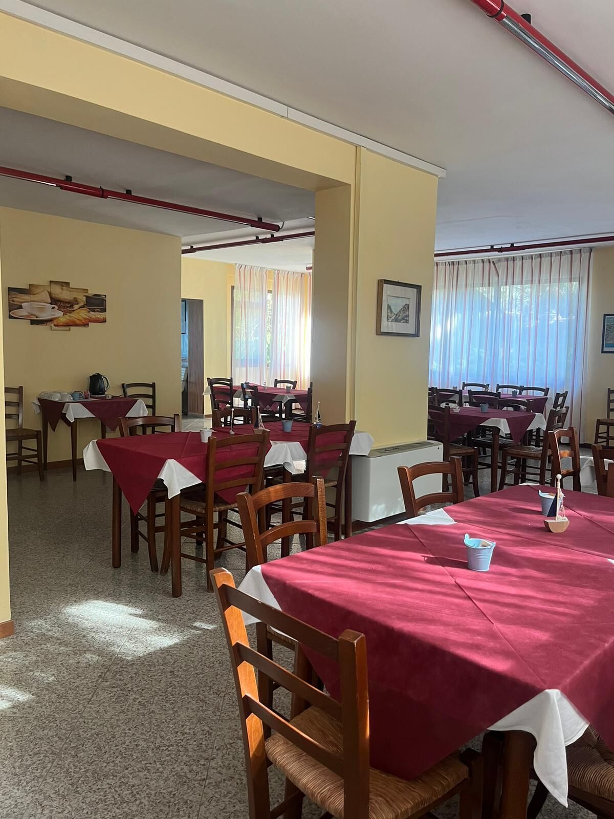 A dining area with multiple tables and chairs, some covered with red tablecloths.