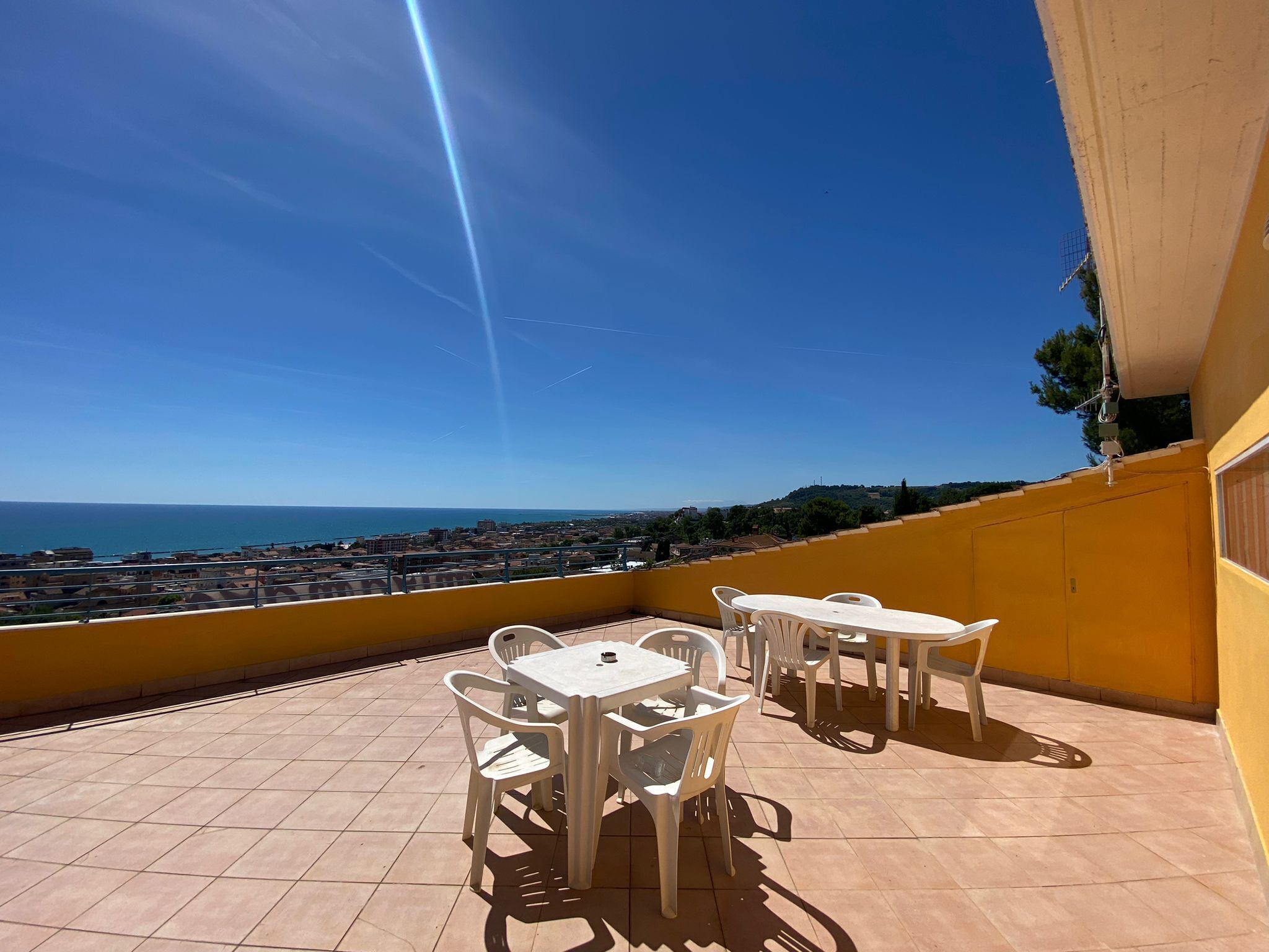 A terrace with white plastic chairs and tables, overlooking a coastal cityscape.