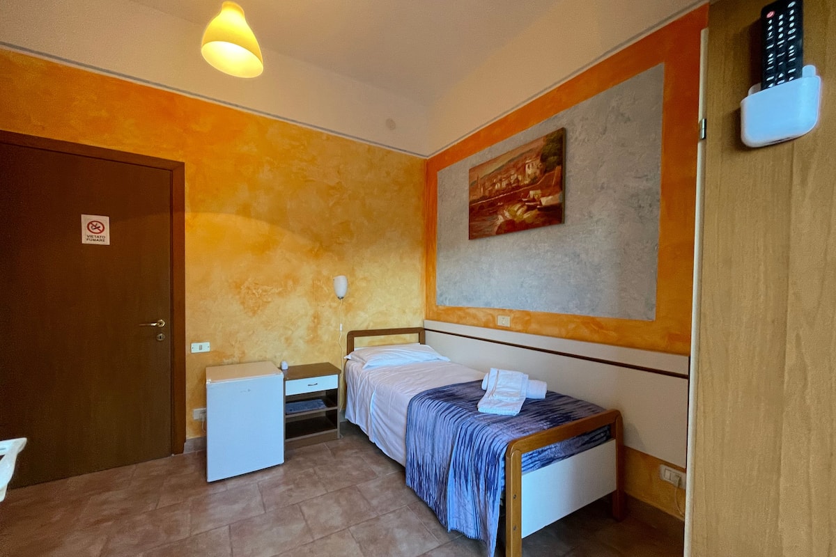 A bedroom with a bed, bedside table, and a painting on the wall.