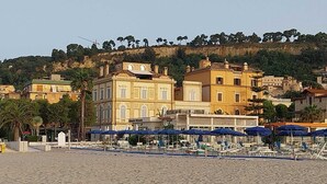 A coastal hotel with multiple floors, outdoor seating with umbrellas, and a view of the hillside. - B&B Miramare Grottammare (Grottammare)