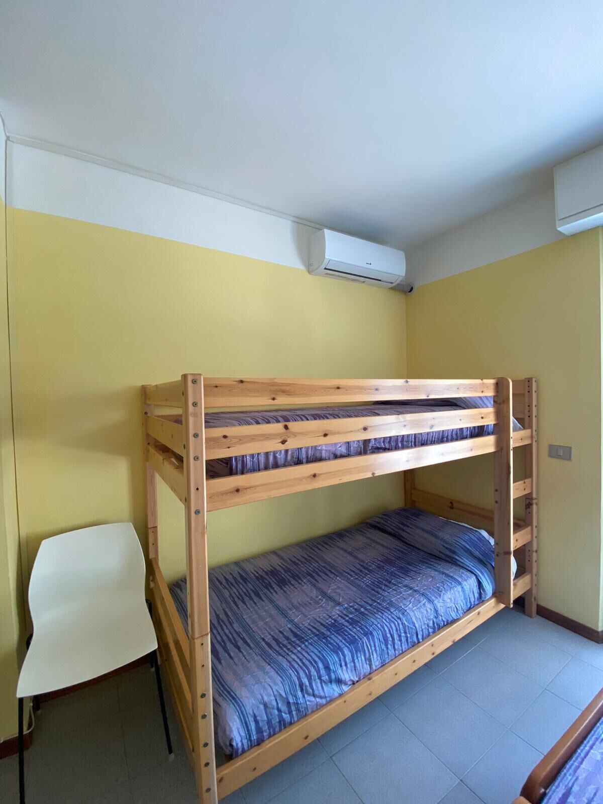 Una cama litera con colchón azul en una habitación con paredes amarillas y techo blanco.