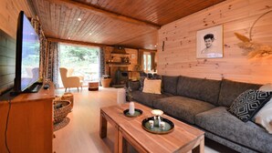 A cozy living room with a wooden ceiling, a sofa, a television, and a fireplace. - Cozy Chalet With Barbecue (Viroinval)