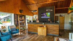 A reception area with wooden paneling, a TV mounted on the wall, and a reception desk. There are two chairs and a small table with a menu or brochure. - Nice Chalet With Dishwasher, on the Veluwe (Otterlo)