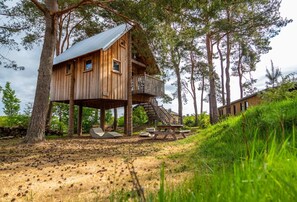 A wooden treehouse with a balcony, surrounded by trees and a picnic area. - Nice Chalet With Dishwasher, on the Veluwe (Otterlo)
