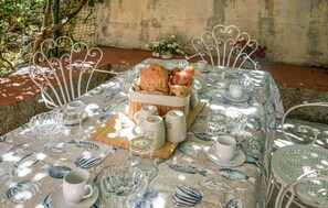 A table set outdoors with a tablecloth featuring a fish pattern, a basket of bread, and several cups and glasses. - Amazing apartment in Monteriggioni (Monteriggioni)