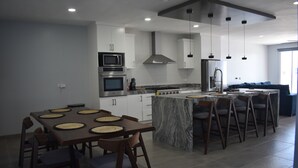 Une cuisine moderne dotée d’un îlot central, d’appareils électroménagers intégrés et de luminaires suspendus.