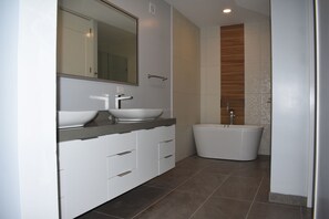 Ein modernes Badezimmer mit einem Doppelwaschtisch, einem großen Spiegel und einer freistehenden Badewanne.