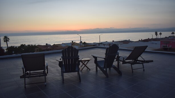 Une terrasse sur le toit avec trois fauteuils Adirondack, une petite table et une vue sur la mer au coucher du soleil.