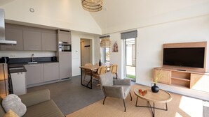 A modern living room with a sofa, a coffee table, and a TV. There is a kitchen with cabinets and appliances, and a dining area with chairs. - Modern Lodge by the Water (Breskens)