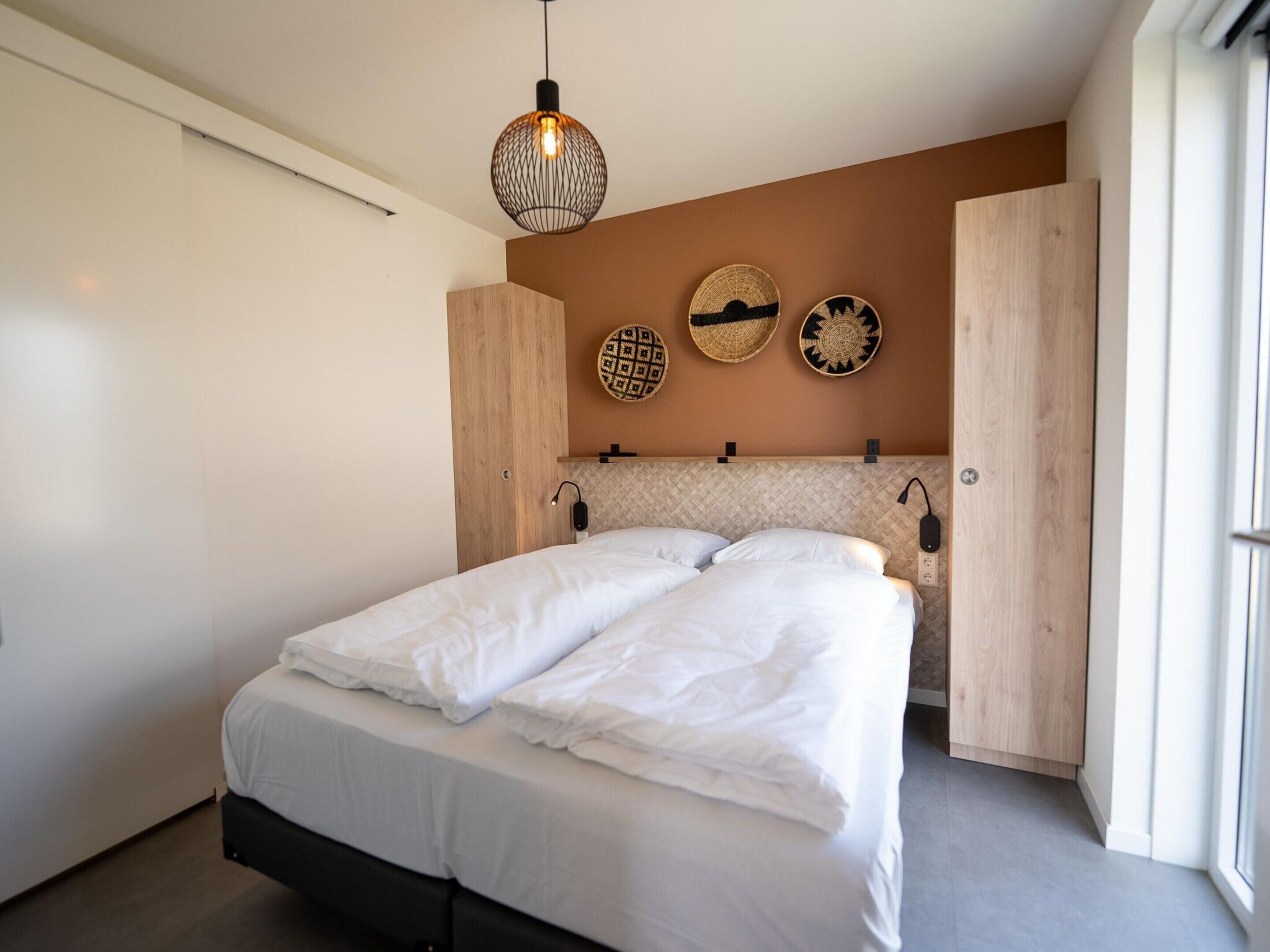 Ein modernes Schlafzimmer mit einem großen Bett, einer Pendelleuchte und Wanddekoration.