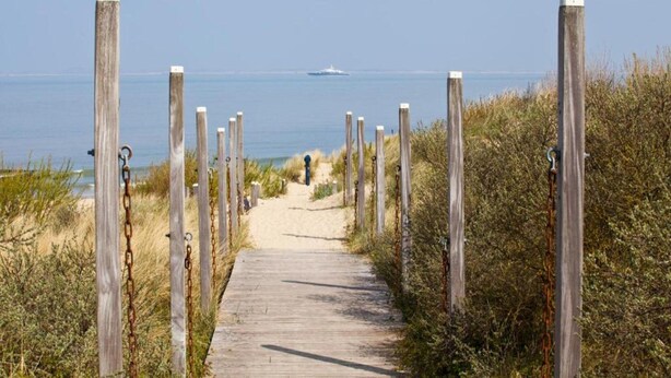A wooden boardwalk leading to a beach with a ship in the distance. - Modern Lodge by the Water (Breskens)