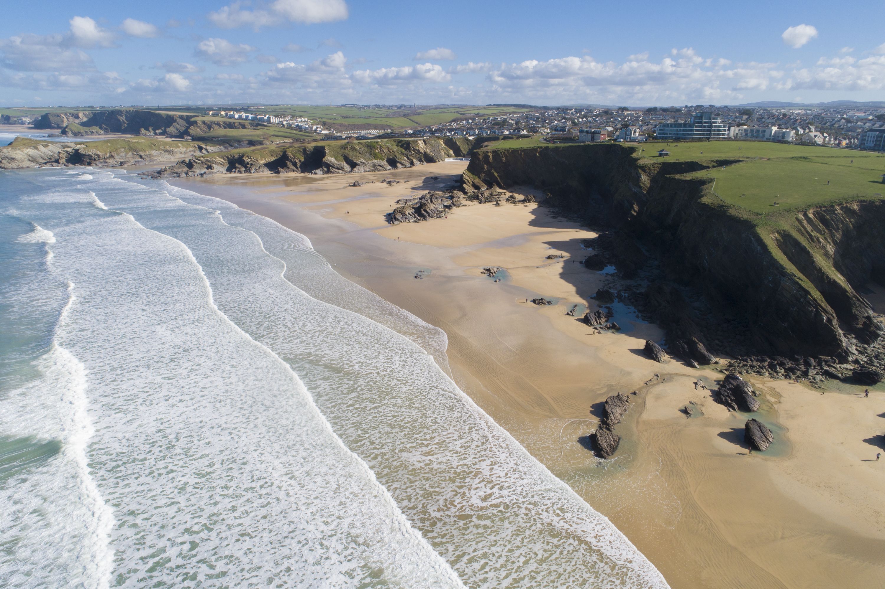 A coastal beach with a sandy shore, rocky cliffs, and a town in the background.