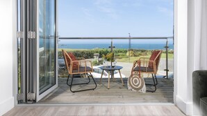 A balcony with two wicker chairs, a small table, and a decorative item. - Sea Breeze -  a sea view apartment just moments from Lusty Glaze Beach (Newquay)