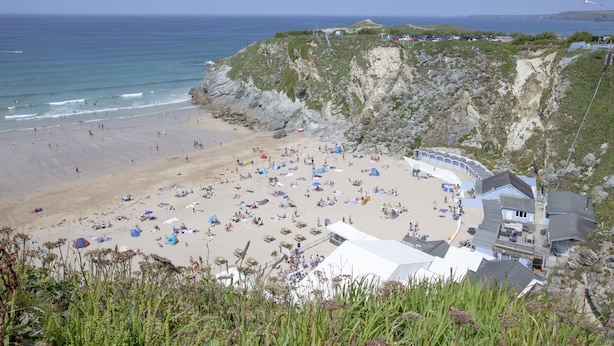 A beach with tents and people, a rocky cliff, and a building with a curved roof. - Sea Breeze -  a sea view apartment just moments from Lusty Glaze Beach (Newquay)