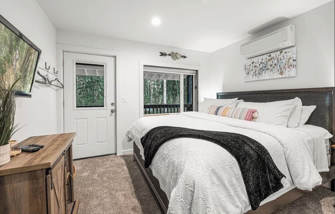 A bedroom with a large bed, a wooden dresser, a door with a window, and an air conditioning unit on the wall.