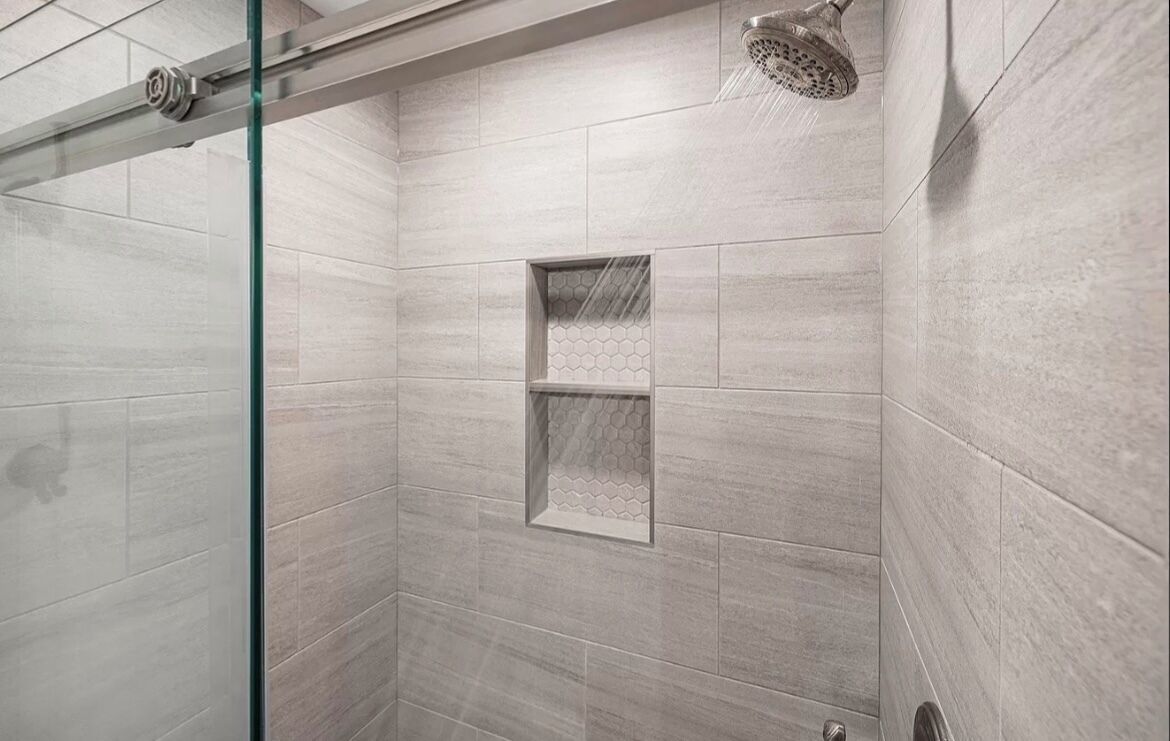 Um chuveiro moderno com porta de vidro, prateleira embutida e chuveiro de efeito chuva.