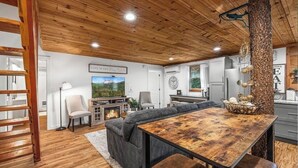 A cozy living room with a wooden ceiling, a fireplace, a large sectional sofa, and a dining table.