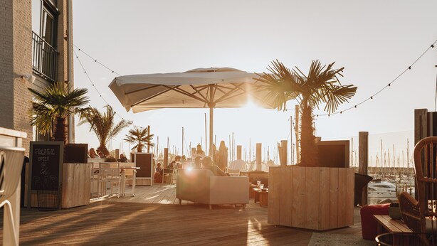 An outdoor seating area with wooden flooring, tables, chairs, and umbrellas. - Holiday Home w/ Sauna Near Beach (Kamperland)