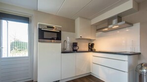A modern kitchen with white cabinetry, a built-in oven, and a stainless steel range hood. - Holiday Home w/ Sauna Near Beach (Kamperland)