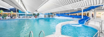 Ein Innenpool mit einer blauen Wasserrutsche, einem überdachten Bereich mit Sitzgelegenheiten und einem Restaurant namens 'Terrazzo'.