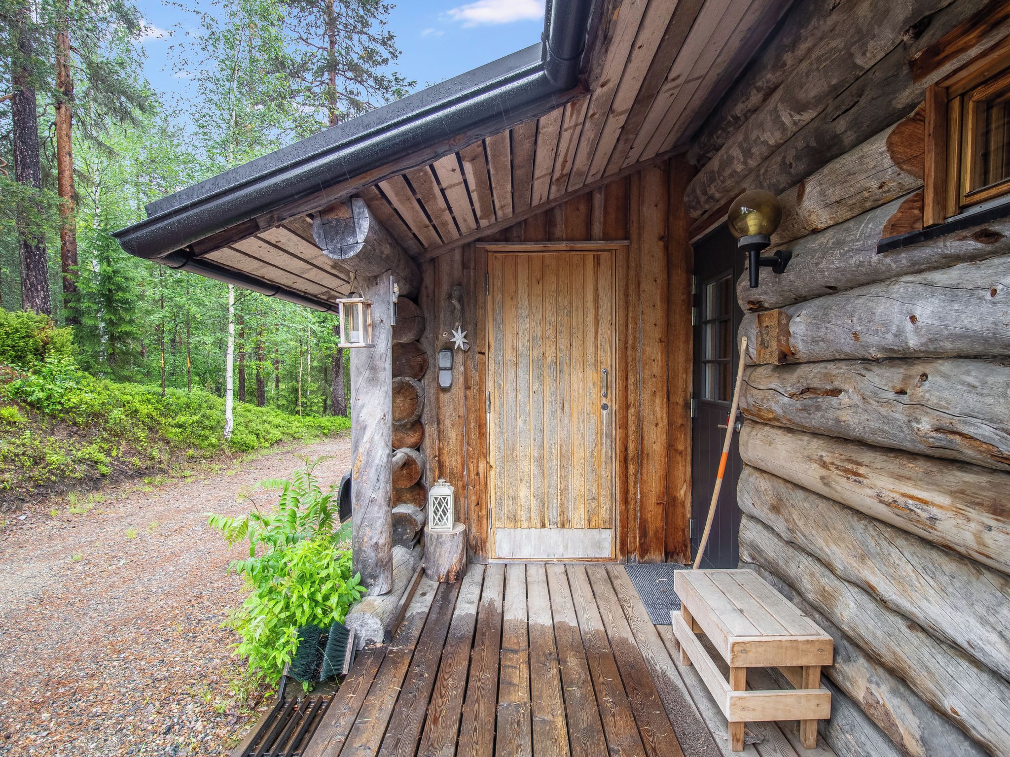 A rustic log cabin with a wooden door, a bench, and a lantern on the porch.