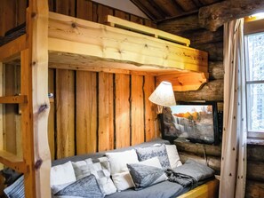 Ein Interieur einer Holzhütte mit einer Couch, Kissen, einer Lampe und einem Fernseher, der eine Wasserfallszene zeigt.