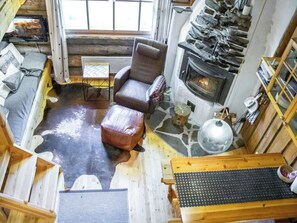 Ein gemütliches Blockhaus-Interieur mit Kamin aus Stein, einer hölzernen Bank und einem Lederhocker.
