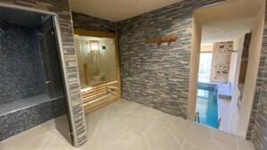 A bathroom with a glass shower enclosure, a stone wall, and a tiled floor.