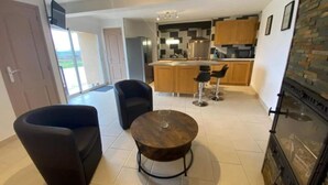 A modern kitchen with wooden cabinets, a central island, and bar stools. There is a dining area with a round table and two chairs.