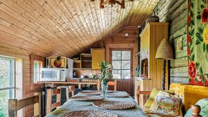 A cozy cabin interior with a dining table set for four, wooden walls, a kitchen area, and a large window.