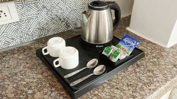A breakfast tray with a kettle, two cups, two spoons, and a pack of coffee creamer on a granite countertop.
