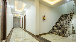 A hallway with a marble floor, a staircase with stone steps, and a fire extinguisher on the wall. - Roomsity Pride (New Delhi)