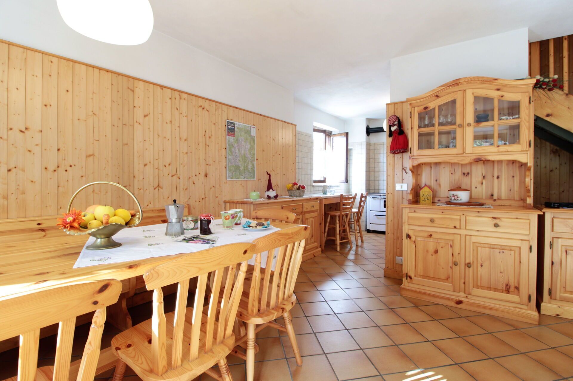 Interior em madeira com mesa de jantar, cadeiras e área de cozinha com armários de madeira e fogão.