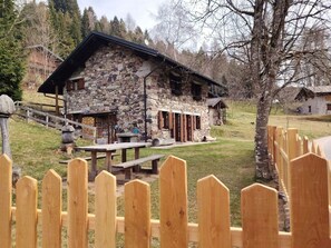 Un edificio de piedra con un porche de madera, una mesa de picnic y una valla de madera.