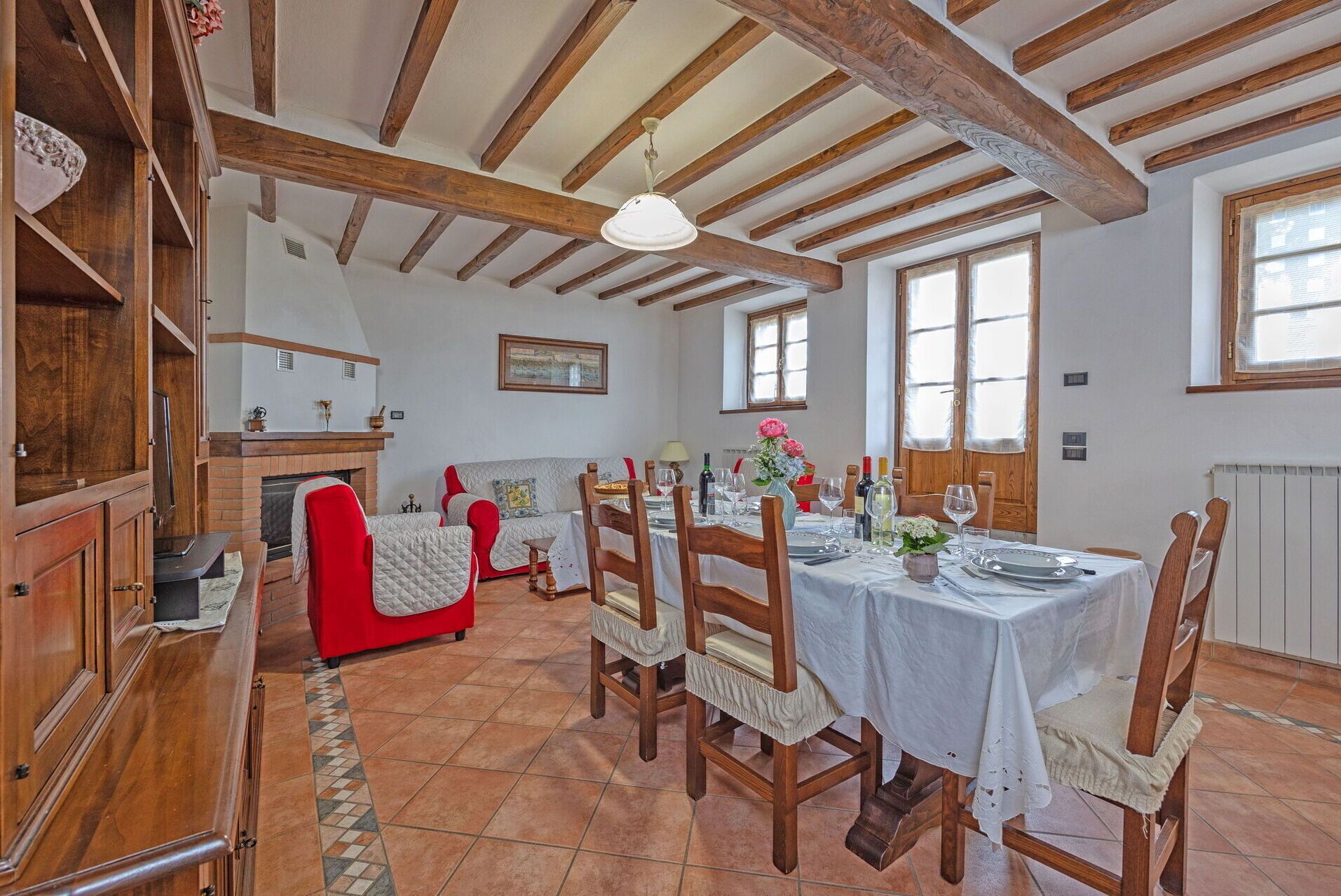 A dining area with wooden beams, a fireplace, and a table set for a meal.