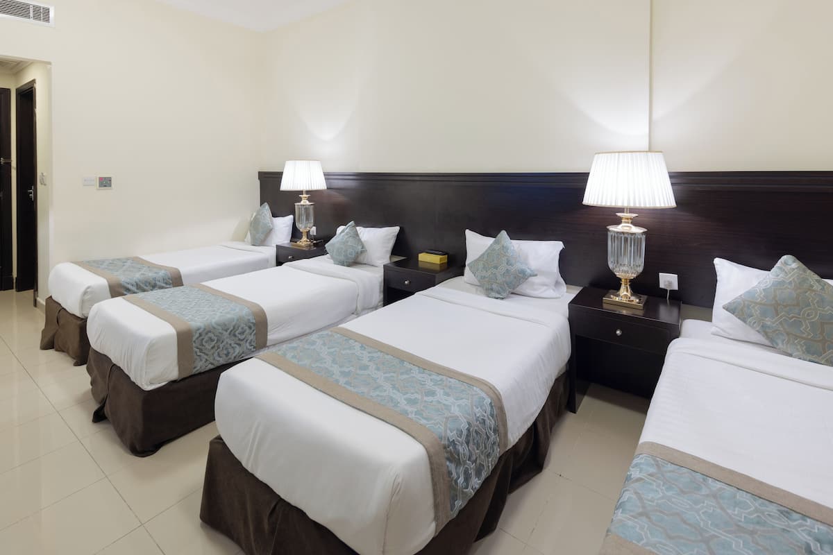 Une chambre d’hôtel avec trois lits simples, chacun étant équipé d’une table de chevet et d’une lampe.