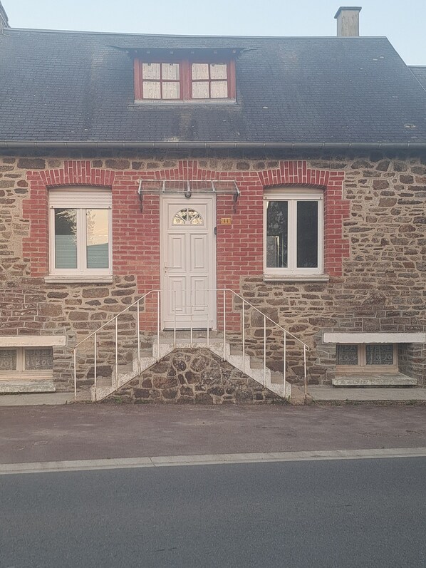 A stone building with a white door, two windows, and a small staircase leading to the entrance.