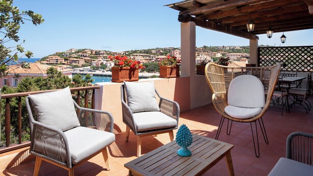 A terrace with wicker chairs, a wooden table, and a view of a coastal town. - Cerbiatta al Molo Apartments by Wonderful Italy (Arzachena)