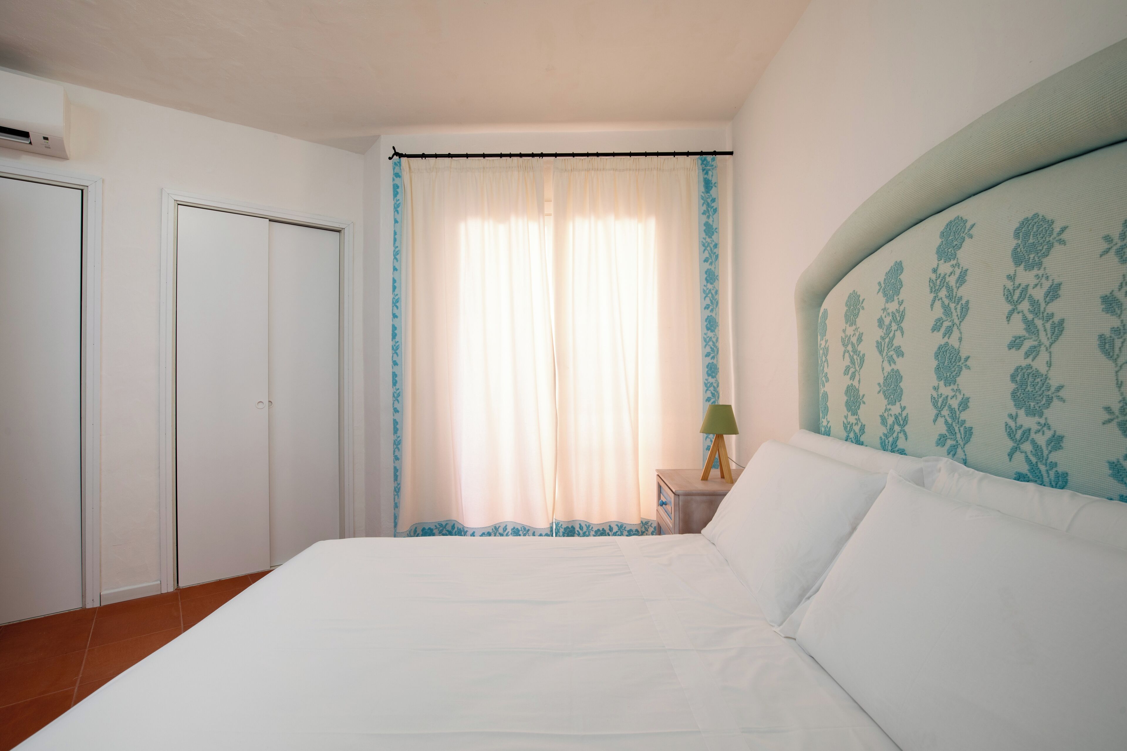 Una camera da letto con un letto, un comodino con una lampada, una finestra con tende e un armadio.